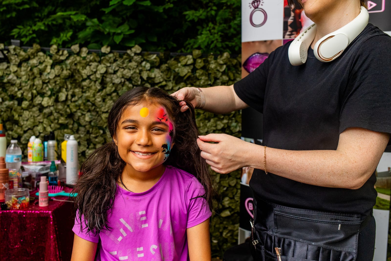 Face painter adding a design to a smiling young guest at an outdoor station