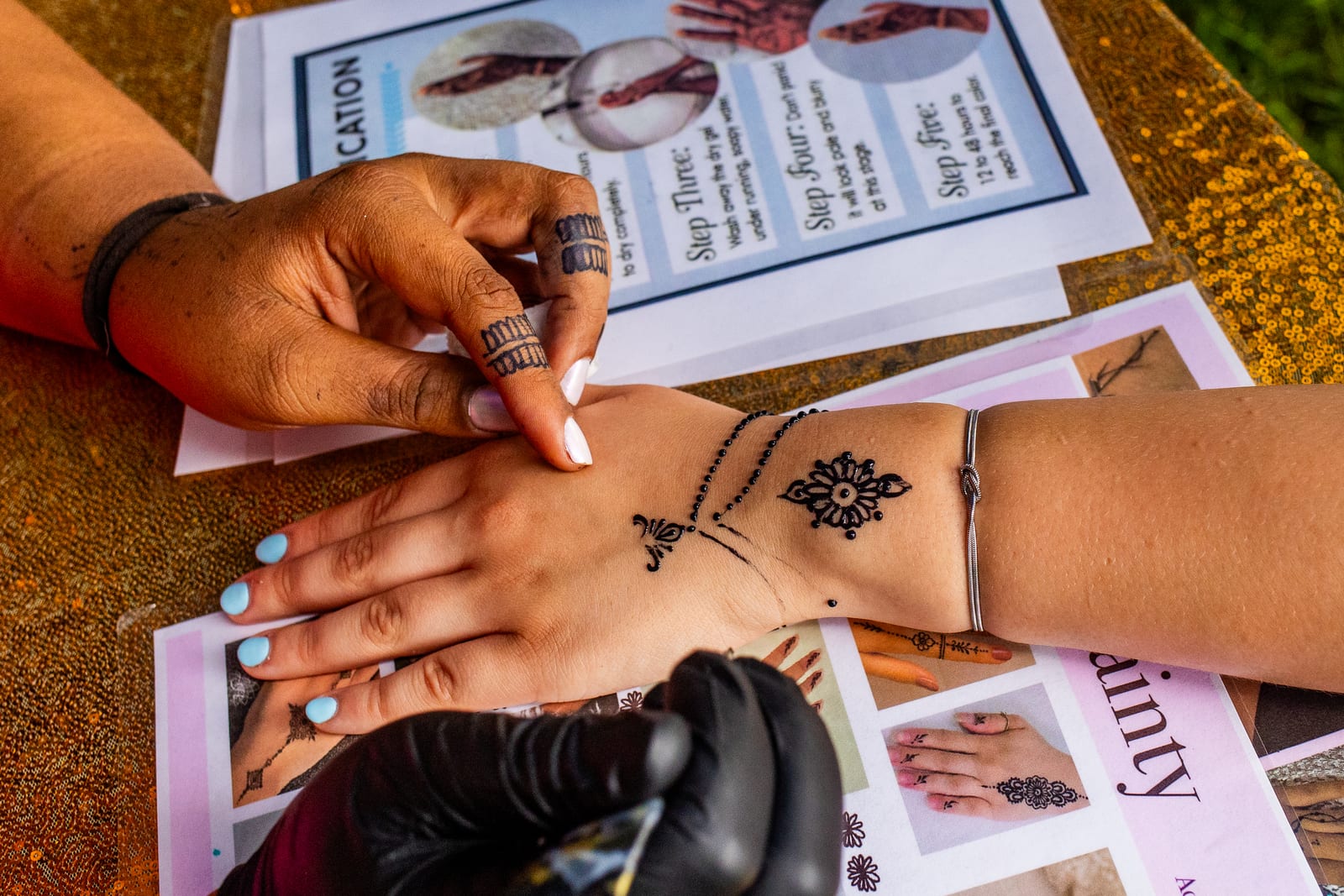 Henna artist drawing a floral design on a guest’s hand at an outdoor table