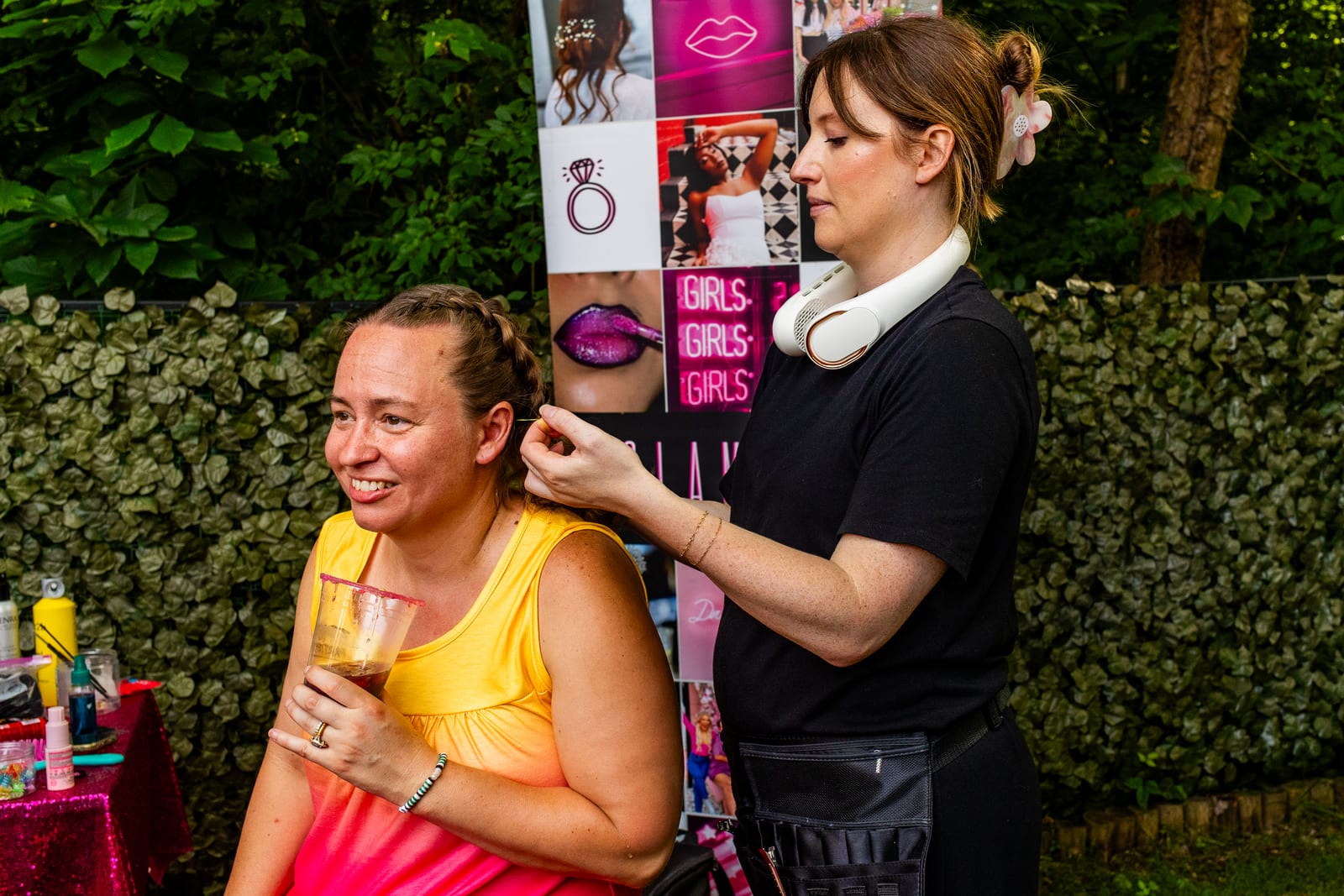 Stylist adding hair tinsel for a guest holding a drink at a garden beauty bar