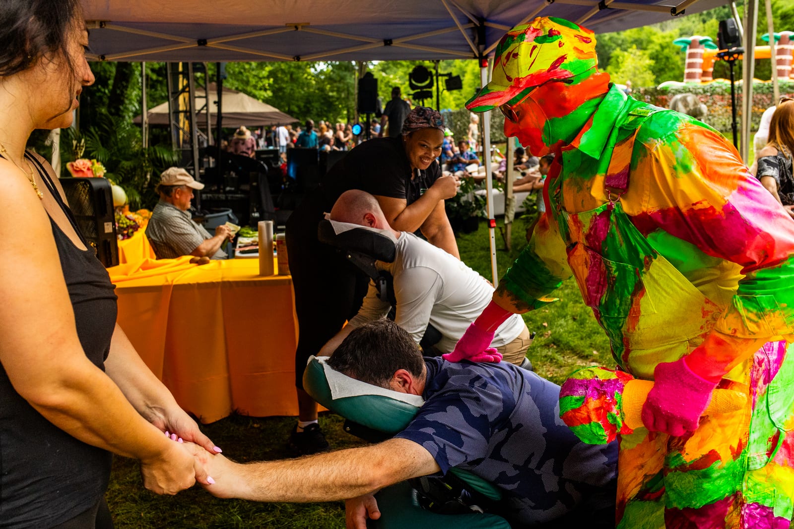 Guest receiving a seated chair massage under a canopy as a costumed performer passes