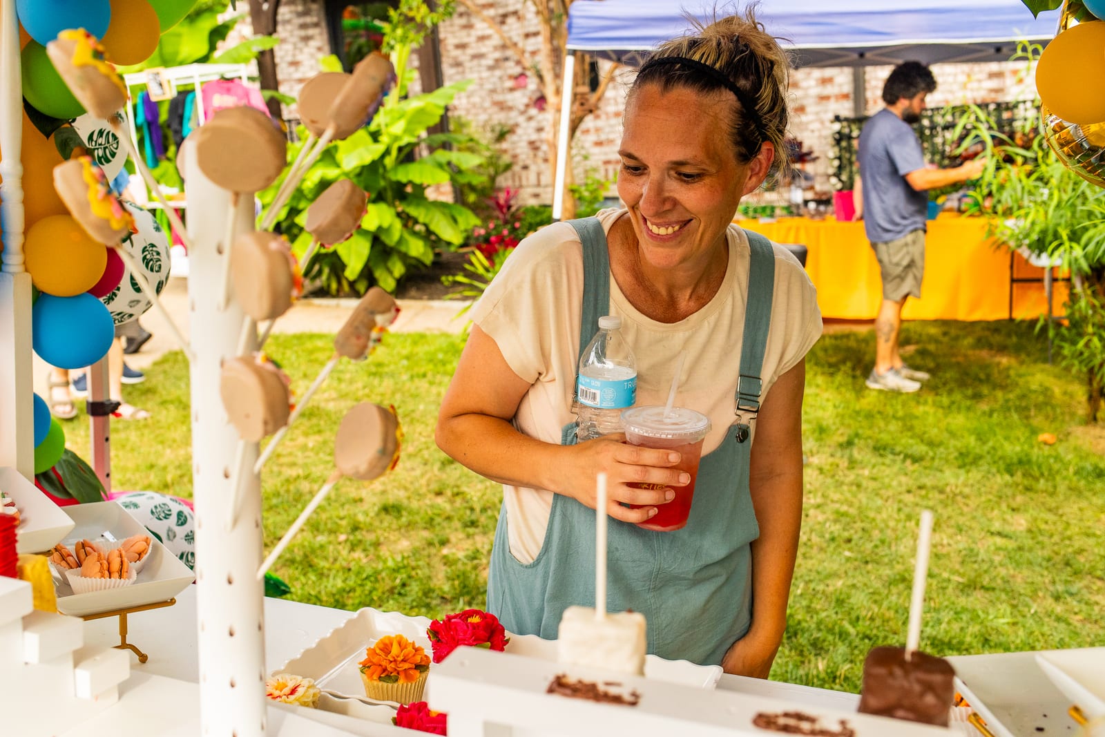 Vendor smiling behind a white dessert cart of treats framed by balloon décor