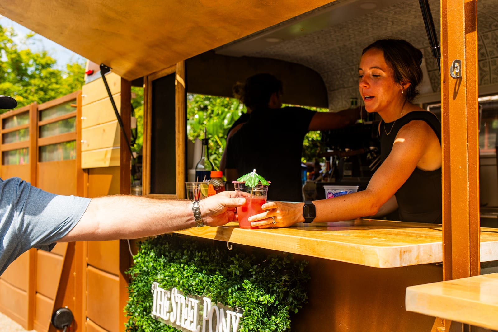 Attendant serving a drink from a wooden mobile bar at an outdoor event