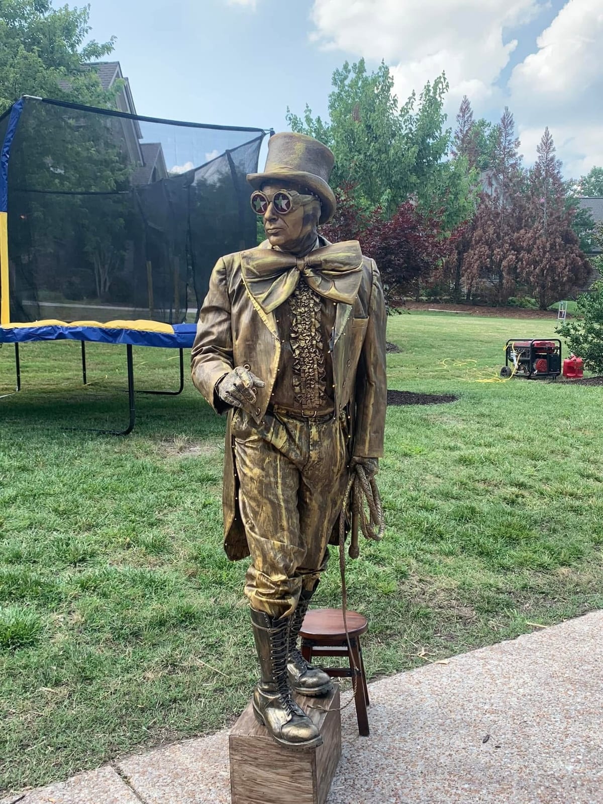 Living-statue performer painted bronze standing motionless on a plinth on a lawn