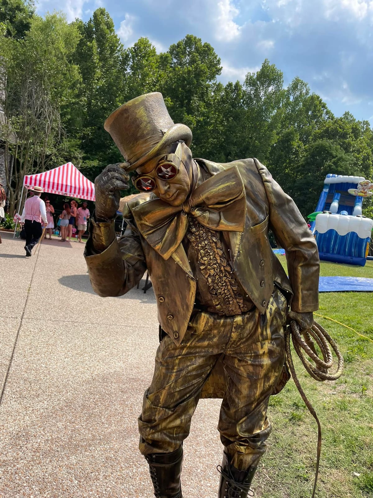 Bronze living-statue performer in a top hat and tails on a garden path