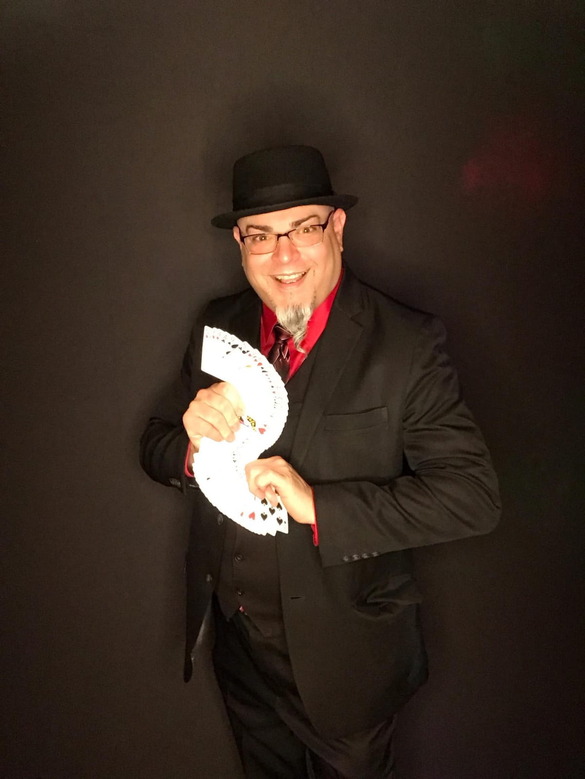 Magician in a bowler hat fanning a deck of playing cards against a dark backdrop