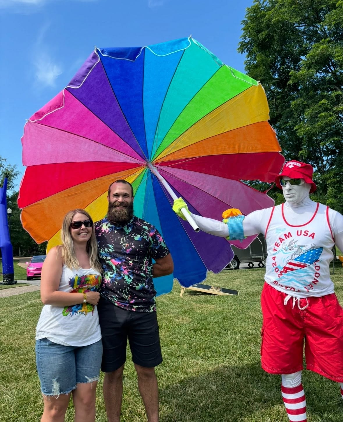 Rainbow-parasol performer posing with two laughing guests on a lawn