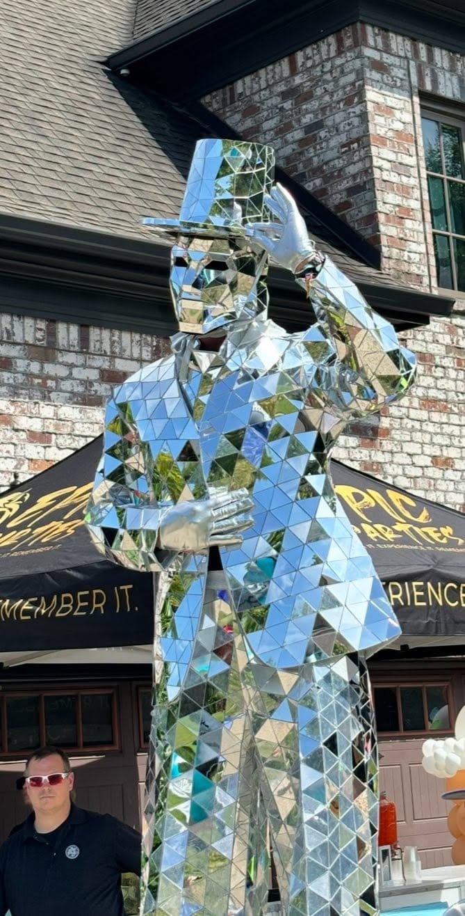 Stilt walker in a mirror-mosaic suit towering over guests on a driveway at a private party