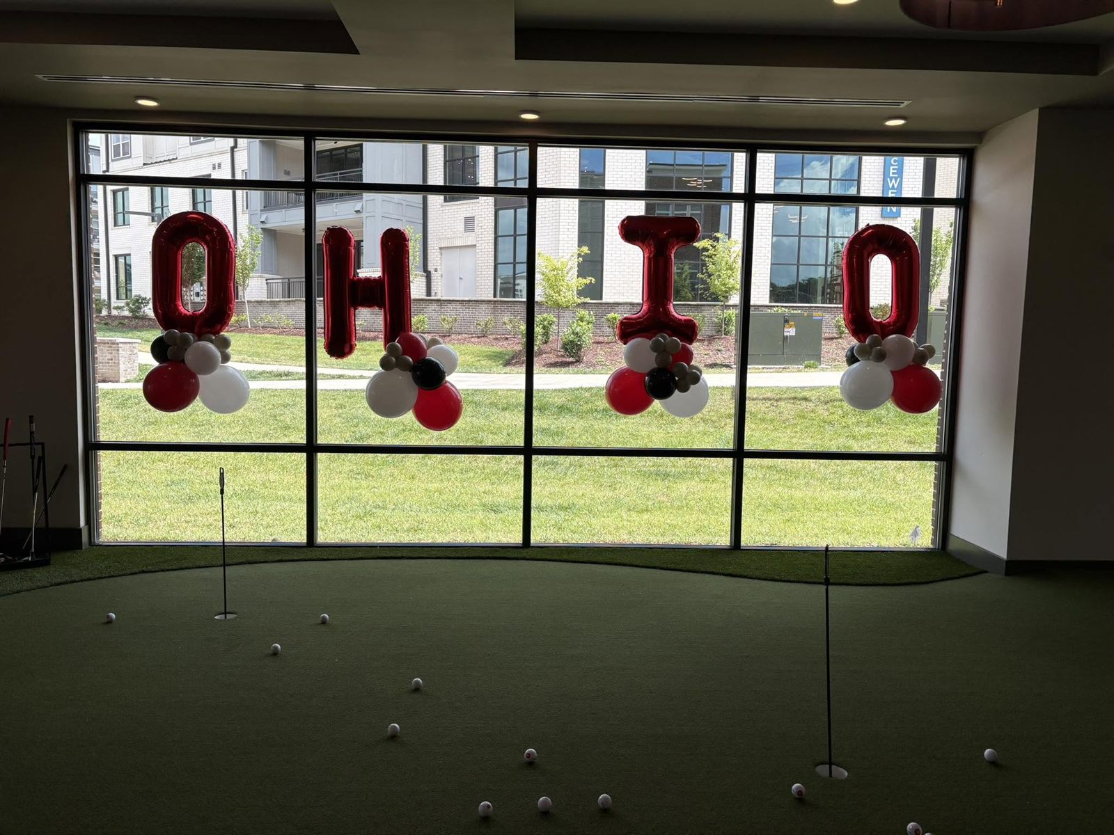 Red foil OHIO balloon letters with scarlet, white and black clusters framing a golf-simulator window