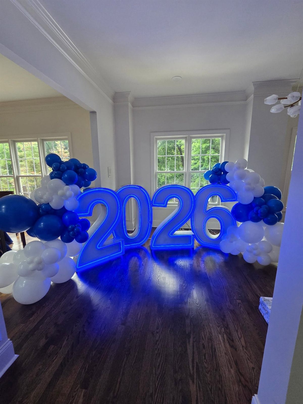 Glowing blue neon 2026 numbers framed by royal-blue and white organic balloon garlands indoors