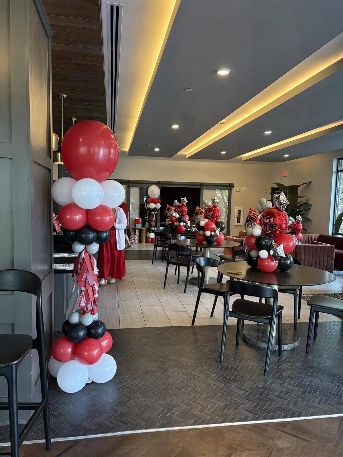 Red, black and white balloon columns and centerpieces styling a lounge with round tables for a grad party
