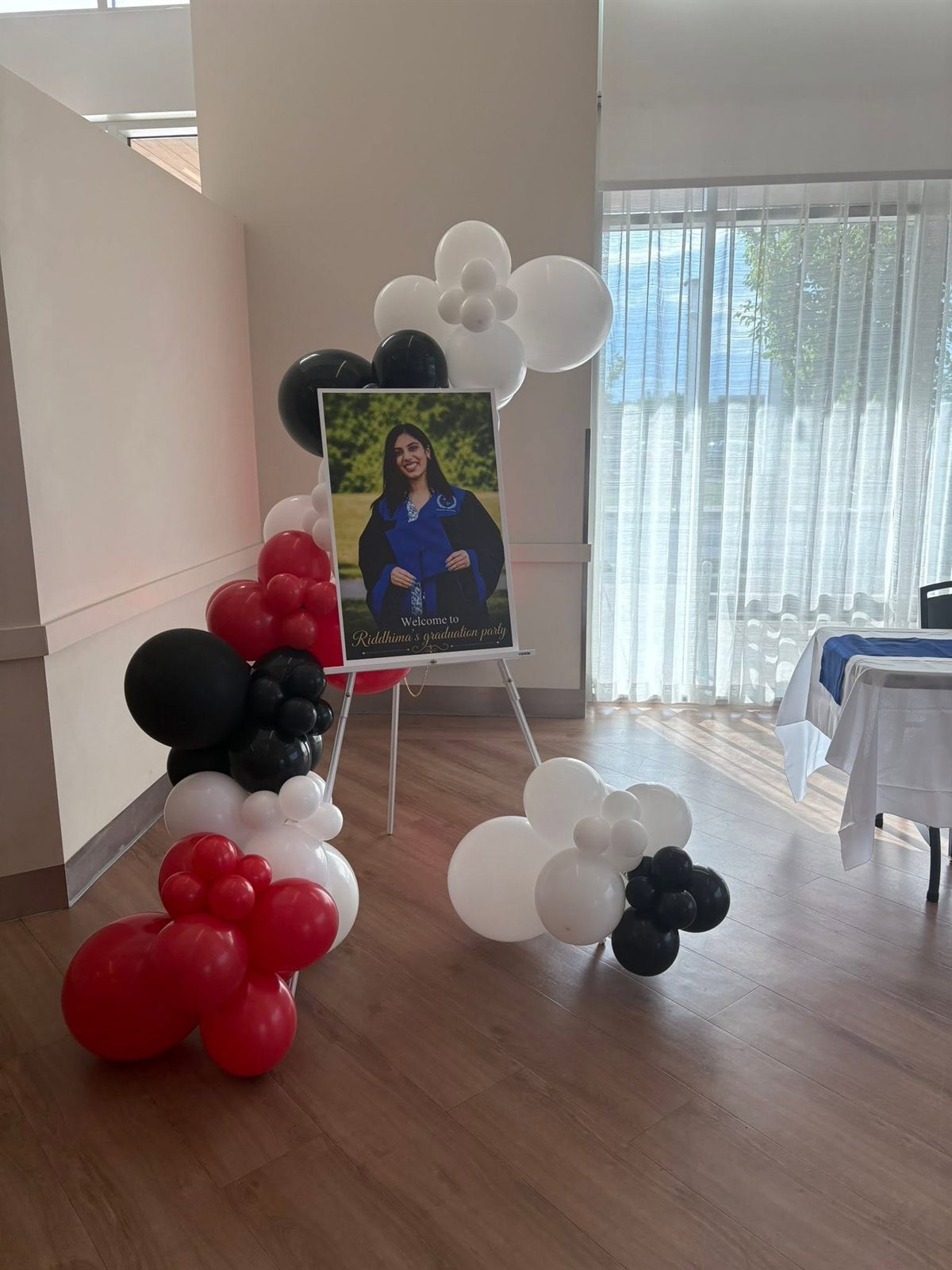 A welcome grad photo sign on an easel framed by red, black and white balloon garland