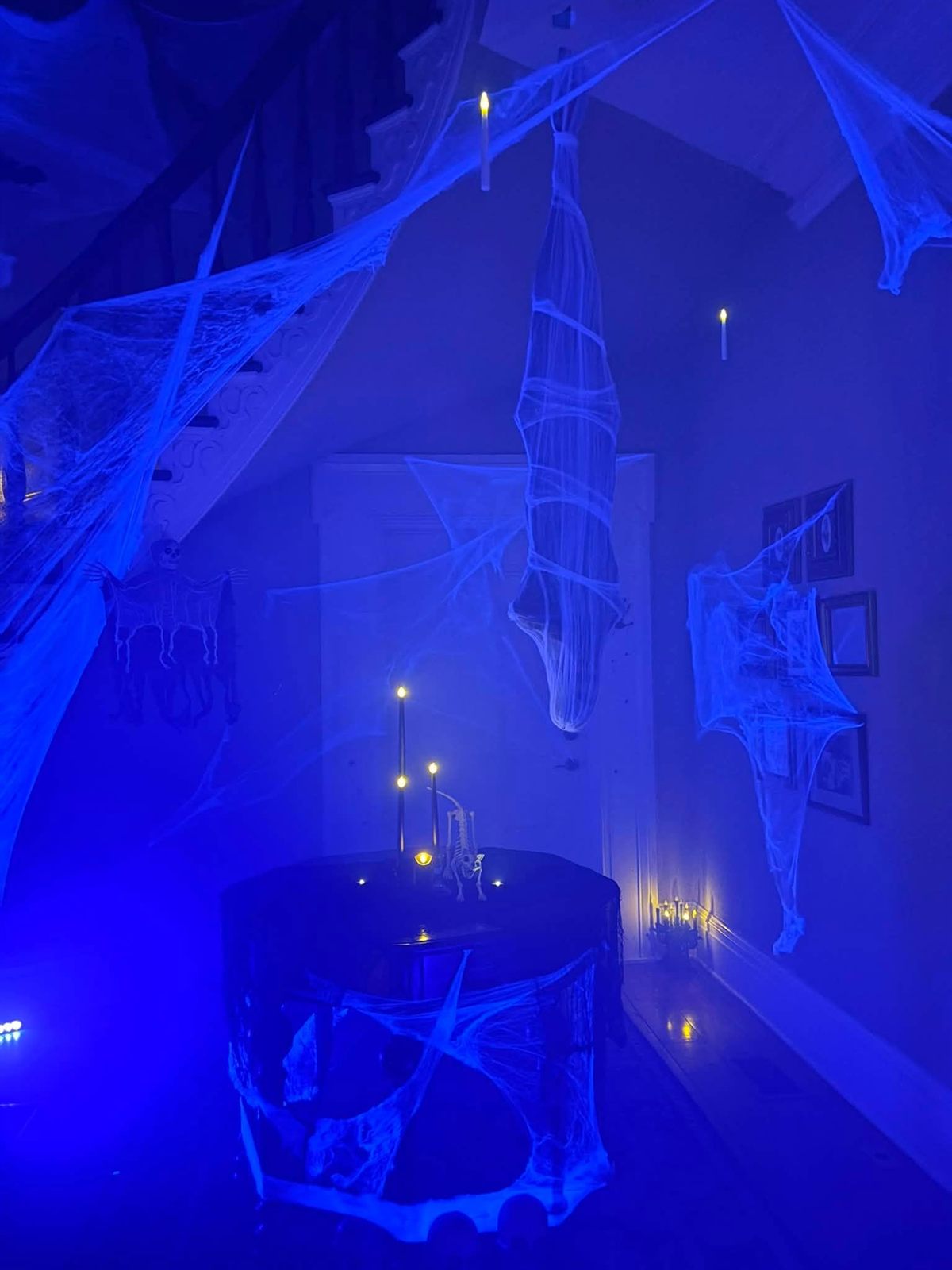 Blacklit foyer draped in cobwebs with a hanging shrouded figure and flameless candles for Halloween
