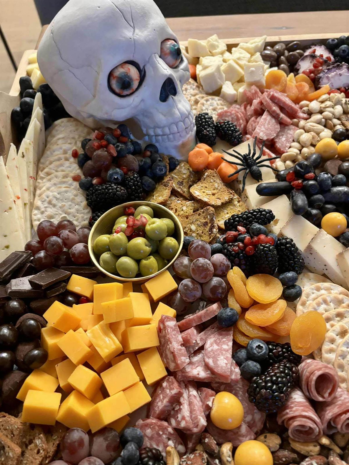 A Halloween charcuterie board with a skull and spider amid cheeses, meats, berries and olives