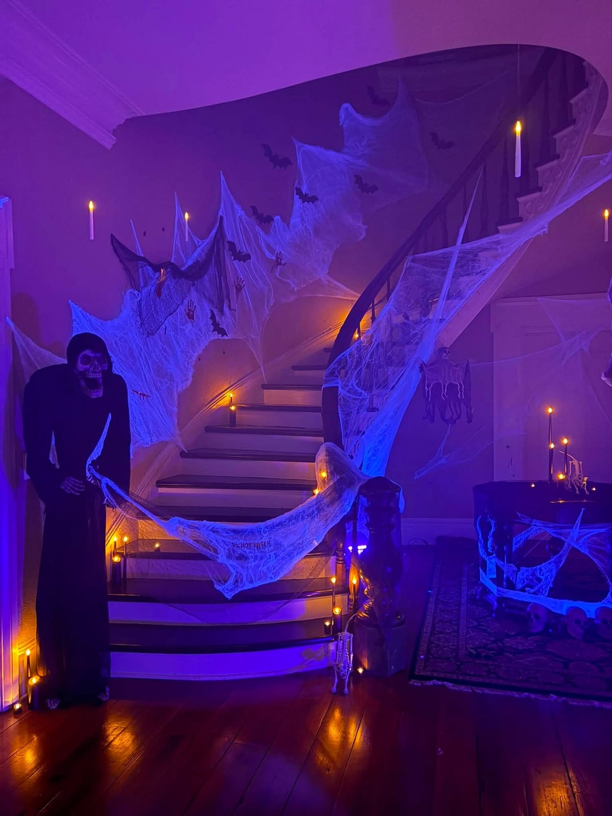 Grand staircase draped in cobwebs and lit purple with a shrouded figure for Halloween