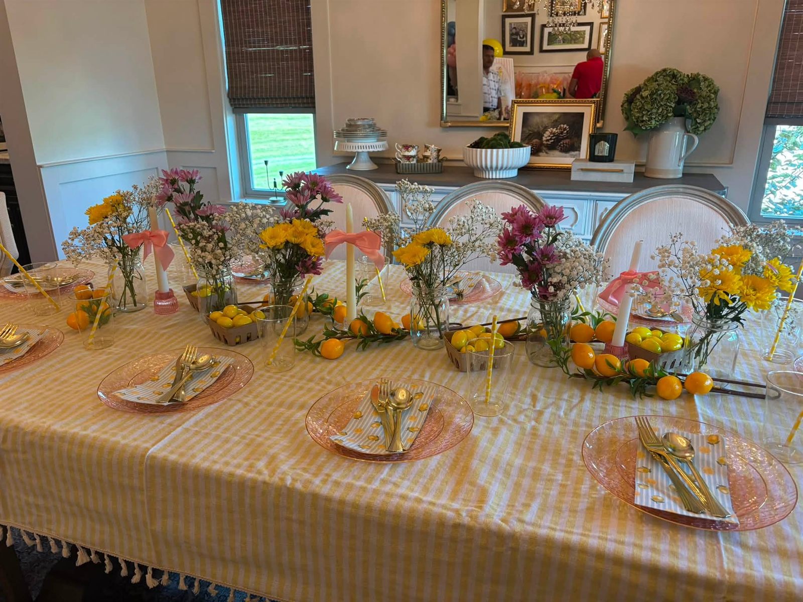 A brunch tablescape with yellow striped linens, pink glass plates, lemon-print napkins, gold cutlery, baskets of lemons and yellow and purple flowers
