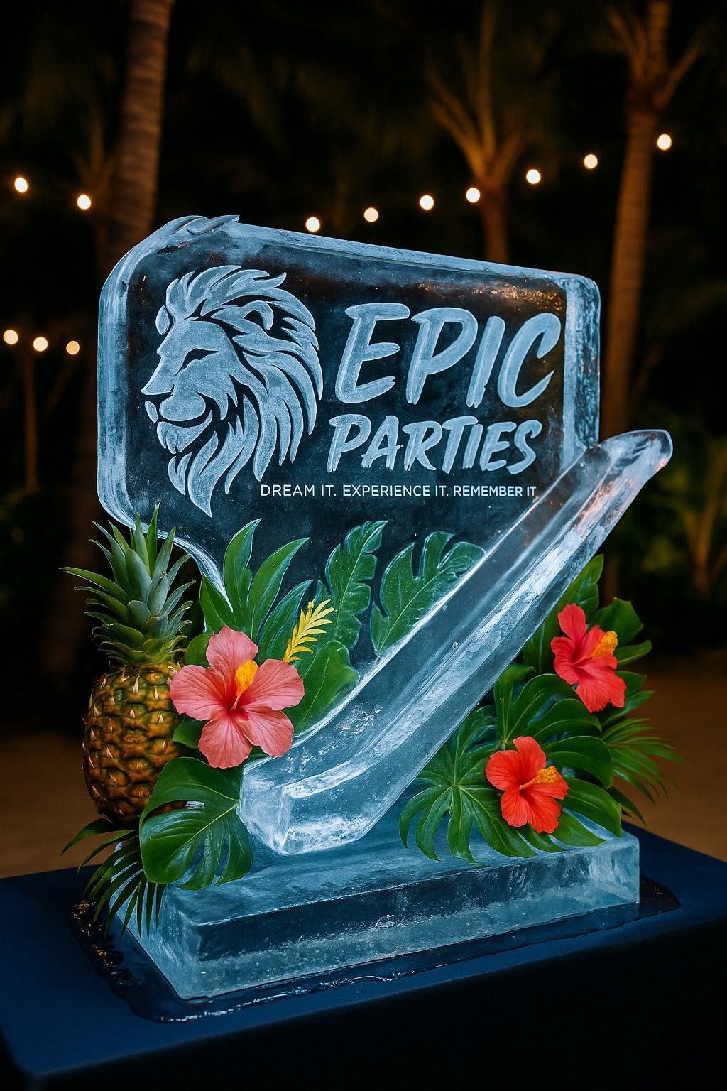 Carved ice sculpture reading EPIC Parties lit blue at night, framed by tropical hibiscus and a pineapple