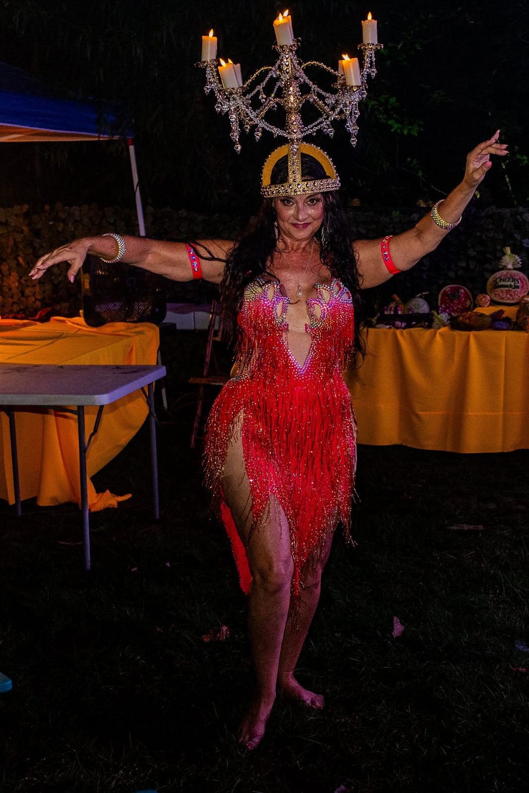 A showgirl balances a lit five-candle candelabra headdress while posing in a red fringe costume