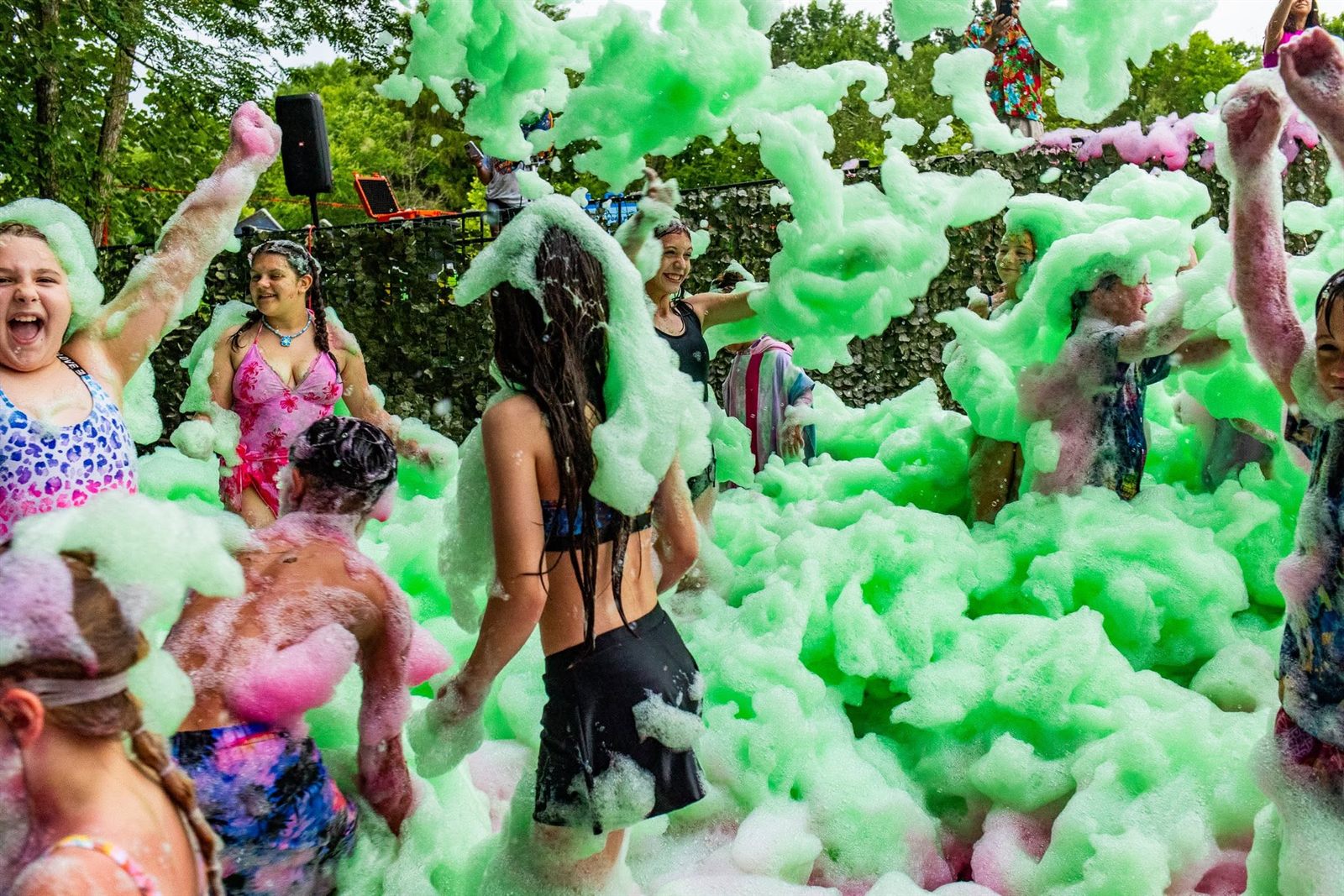 Guests dance and cheer waist-deep in billowing green foam at an outdoor foam party