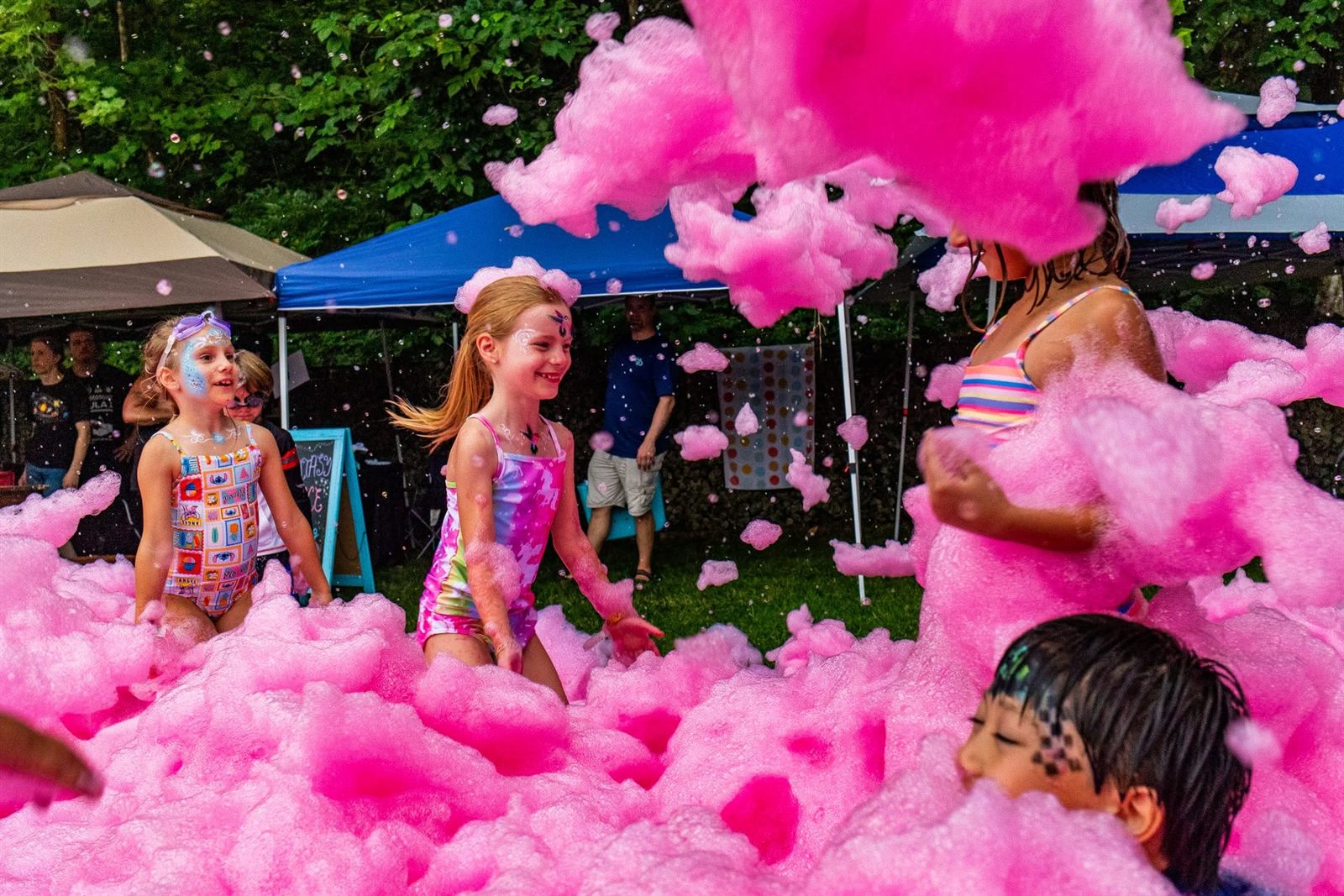 Children in swimsuits laugh and play surrounded by mounds of bright pink foam outdoors