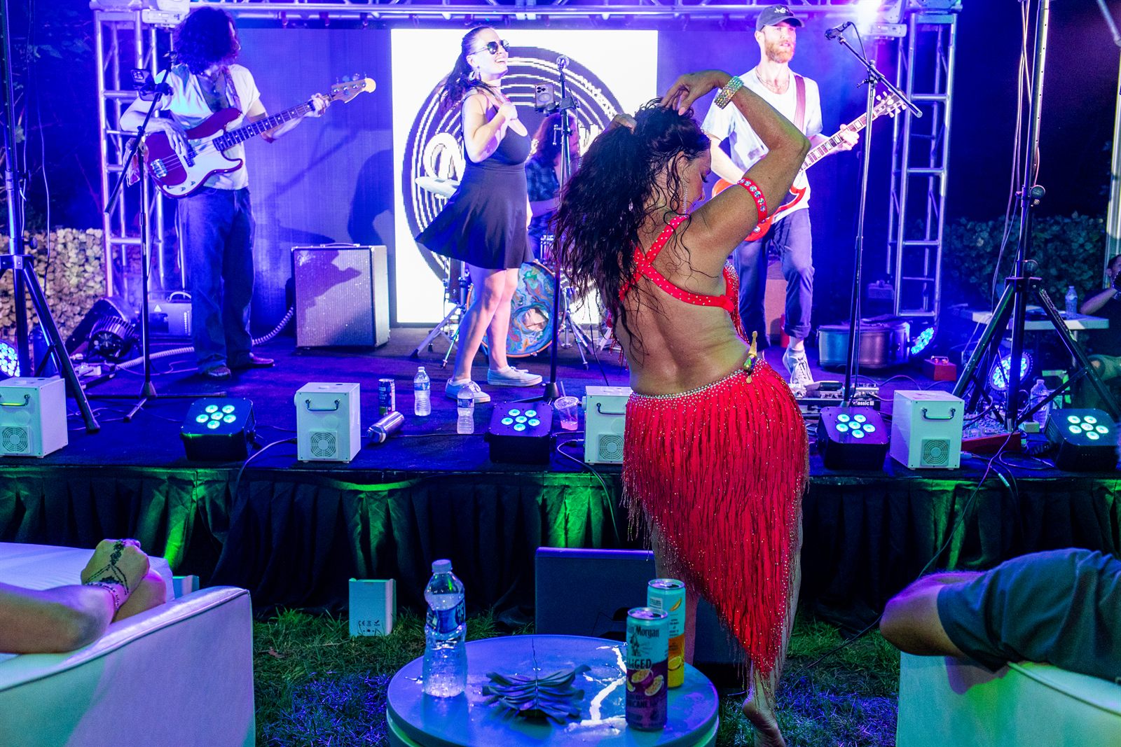 Dancer in a red grass skirt spins with arm raised before a live band bathed in deep blue stage light