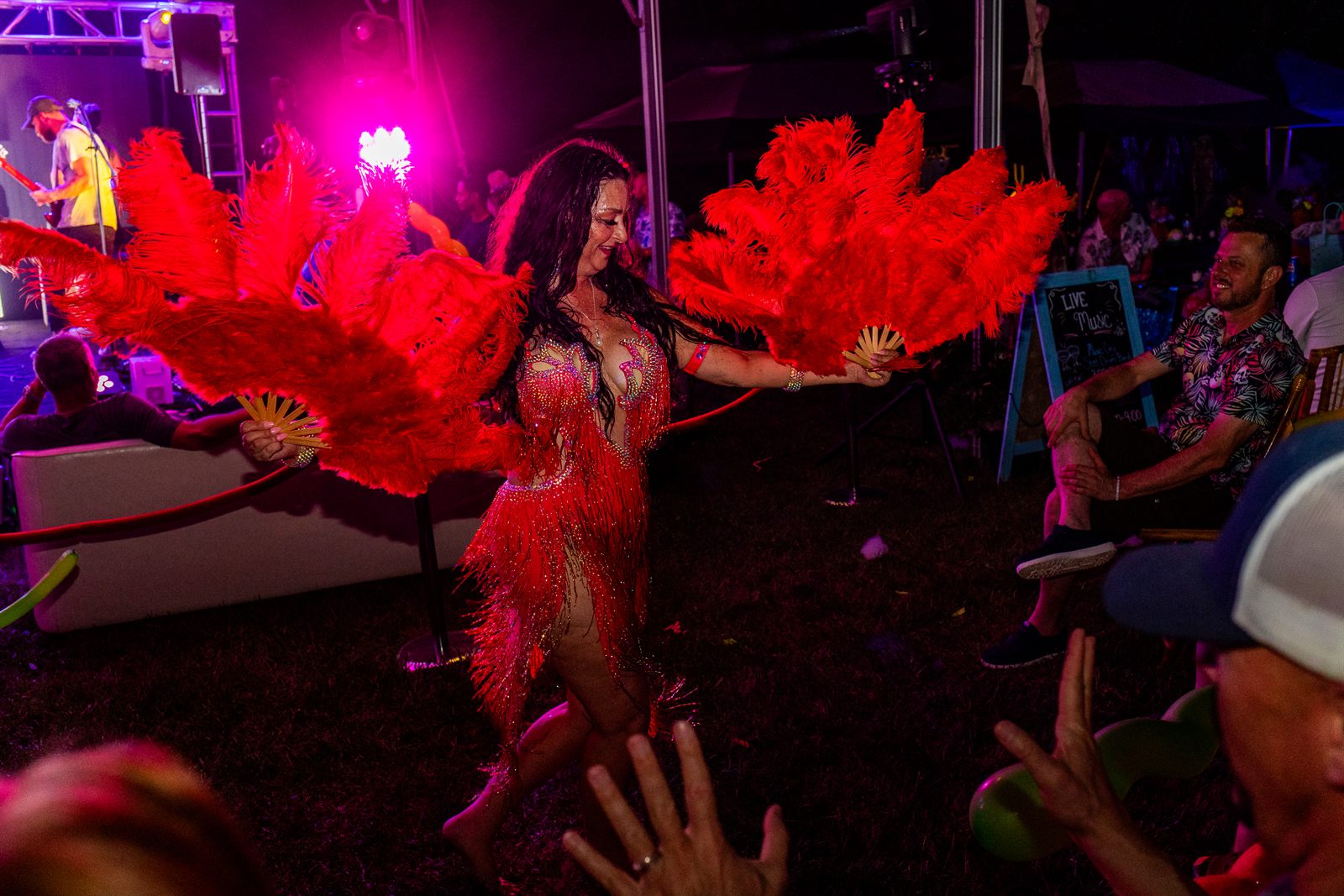 Showgirl dancer in a red sequined costume performing with giant red feather fans among seated guests