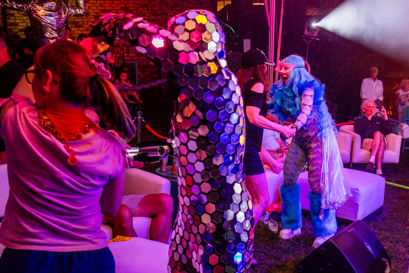 Mirror-mosaic costumed performer and a blue-haired sea-creature dancer entertaining guests under a spotlight
