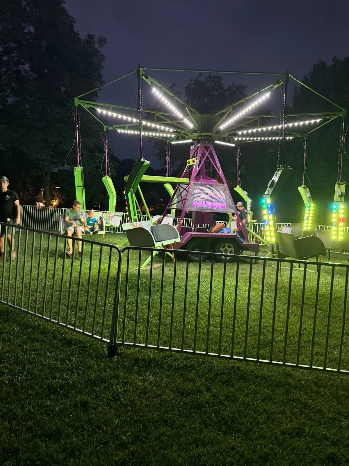 Illuminated fairground swing ride glowing against a deep blue sky at dusk on a private lawn