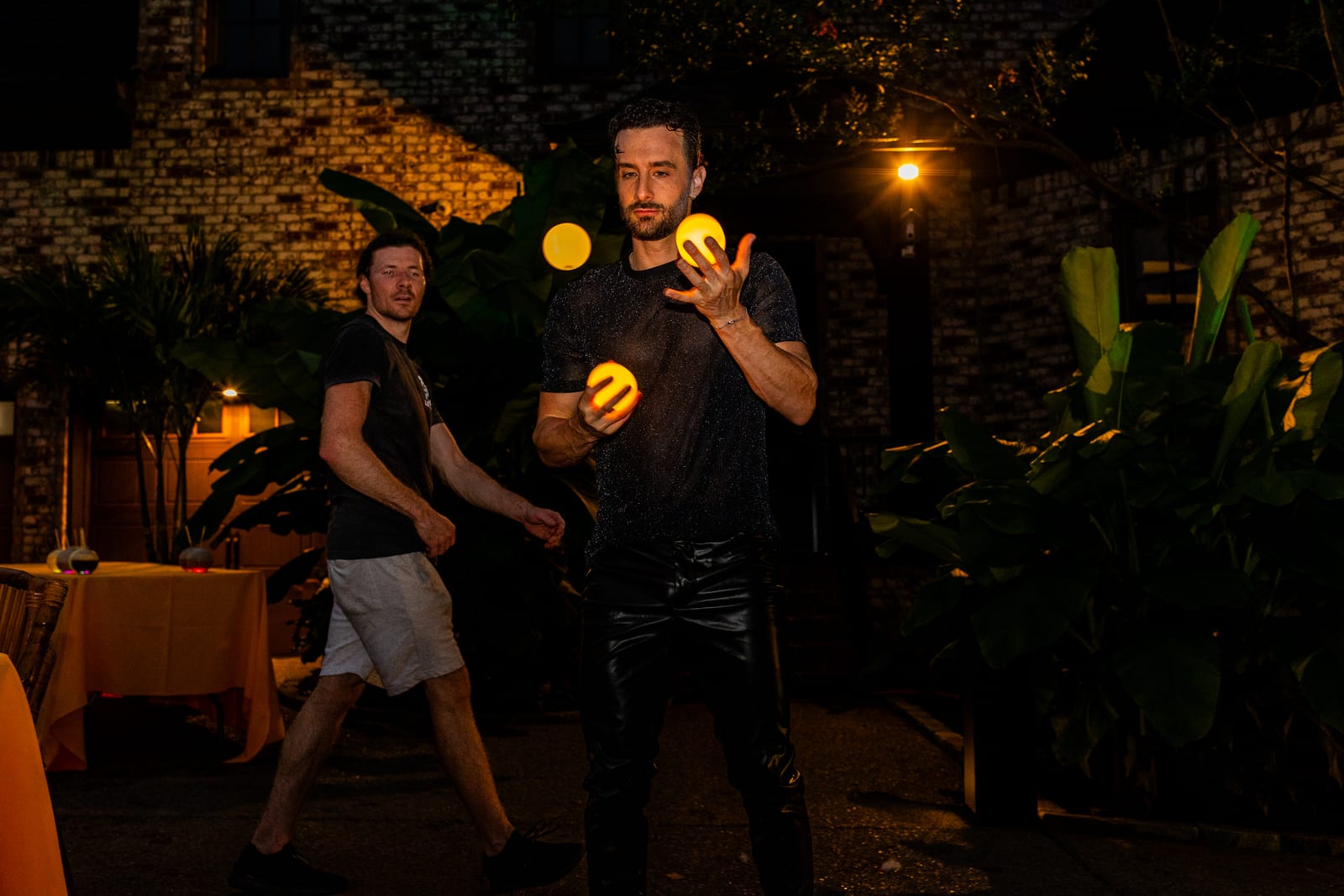 Two performers juggling glowing orbs in the dark beside a lit terrace