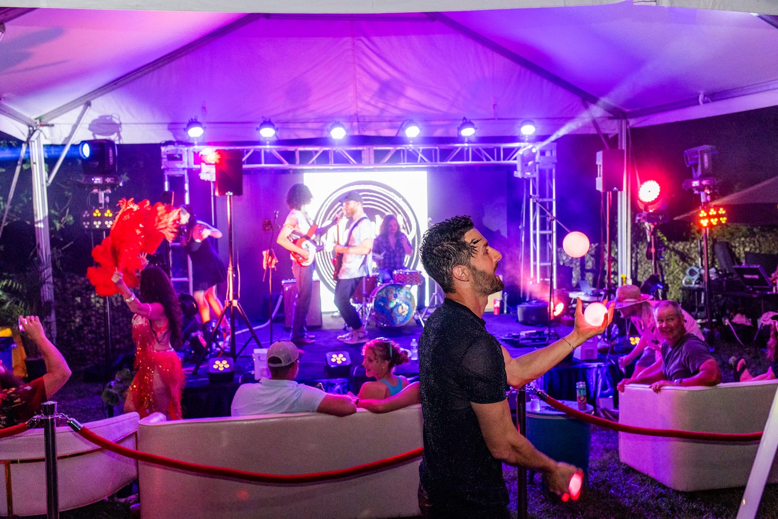 Purple-lit marquee lounge with a juggler, live band and guests on white sofas