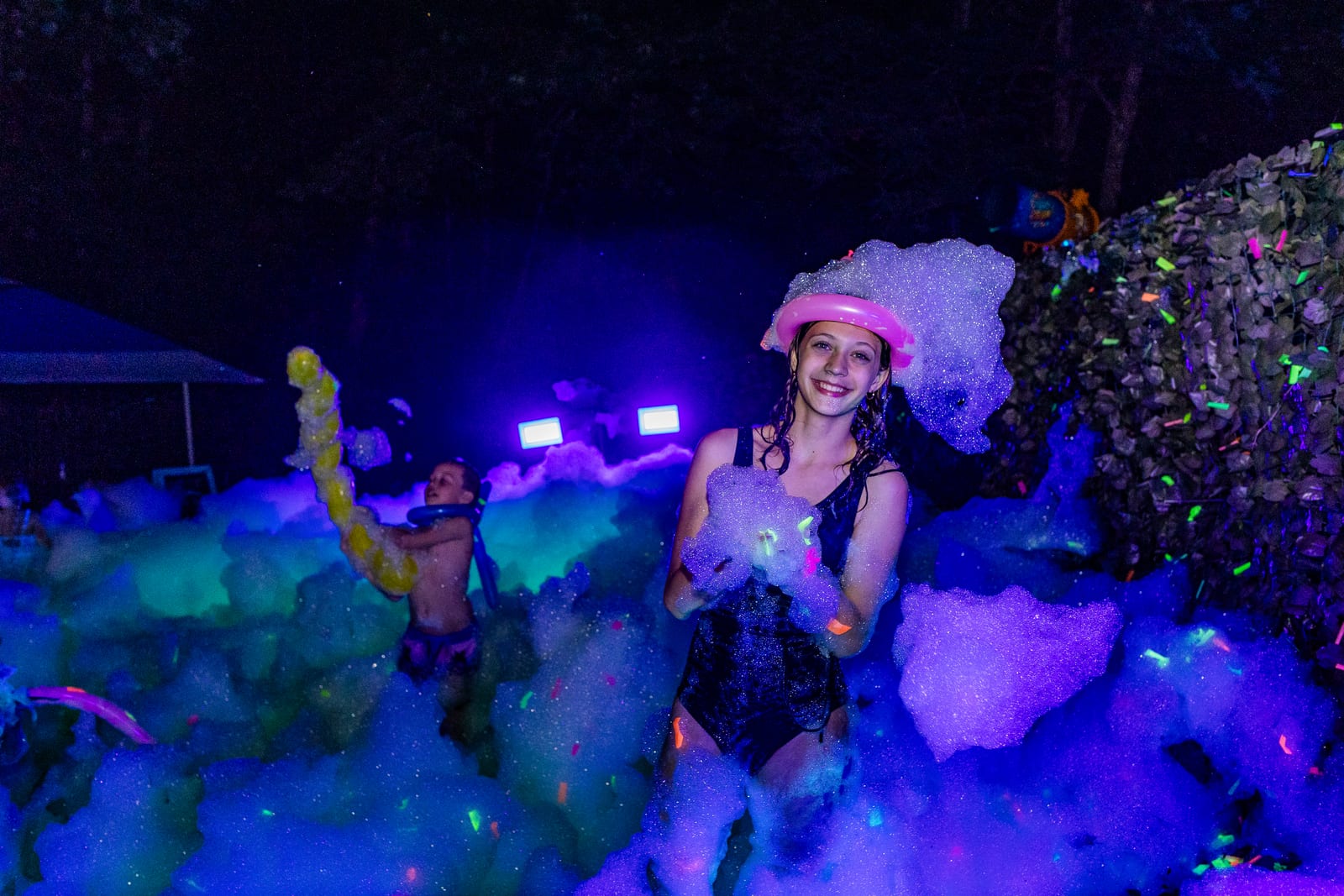 Guest wearing a crown of glowing foam under blue blacklight at a night foam party