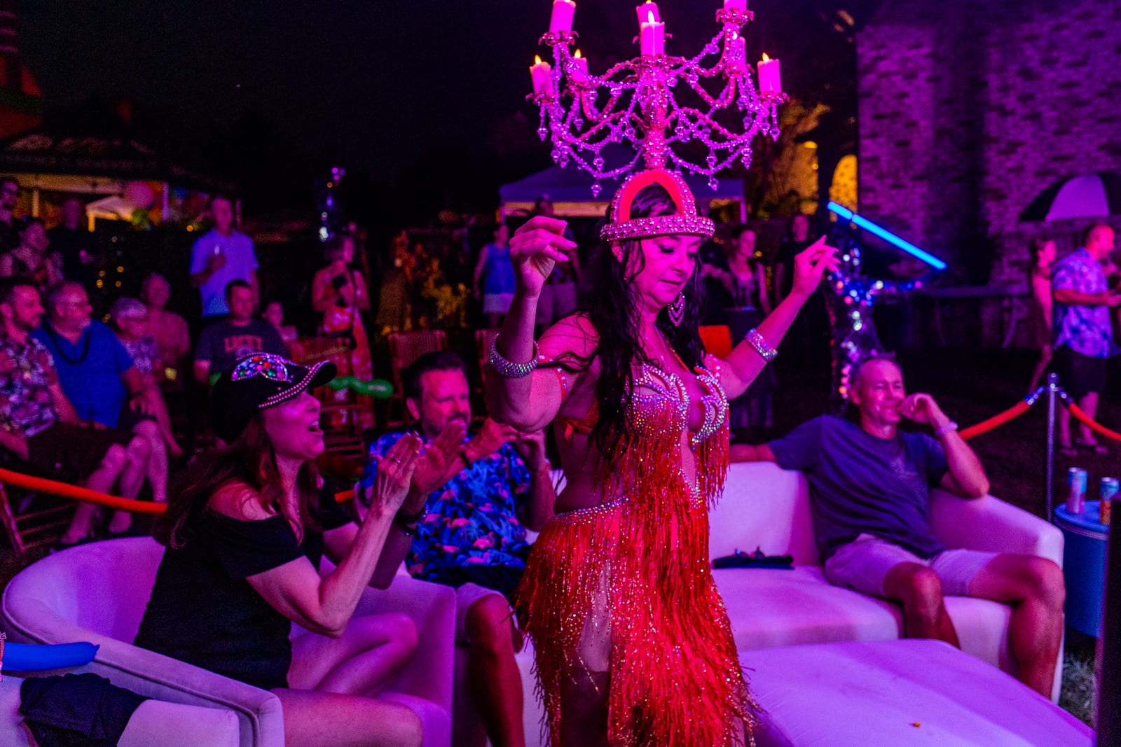 Showgirl in red fringe performing beneath a lit chandelier for seated guests
