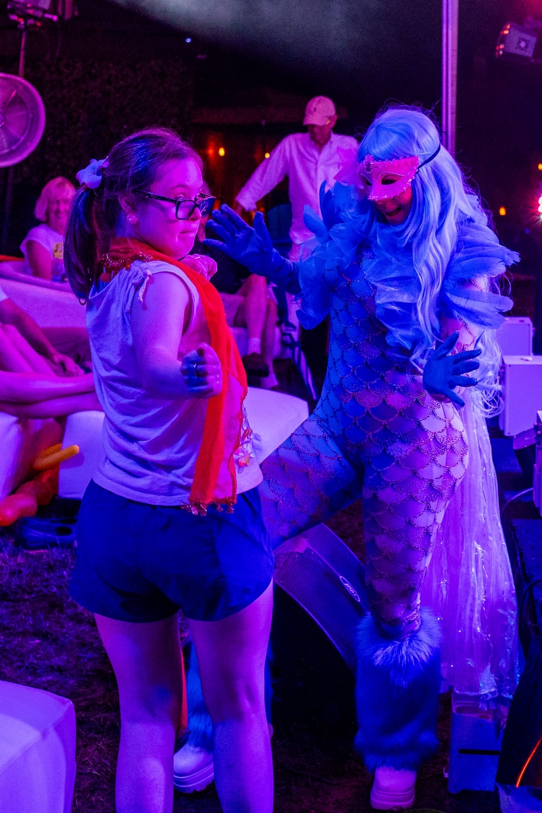 Costumed sea-creature performer in shimmering blue greeting a guest under stage lights