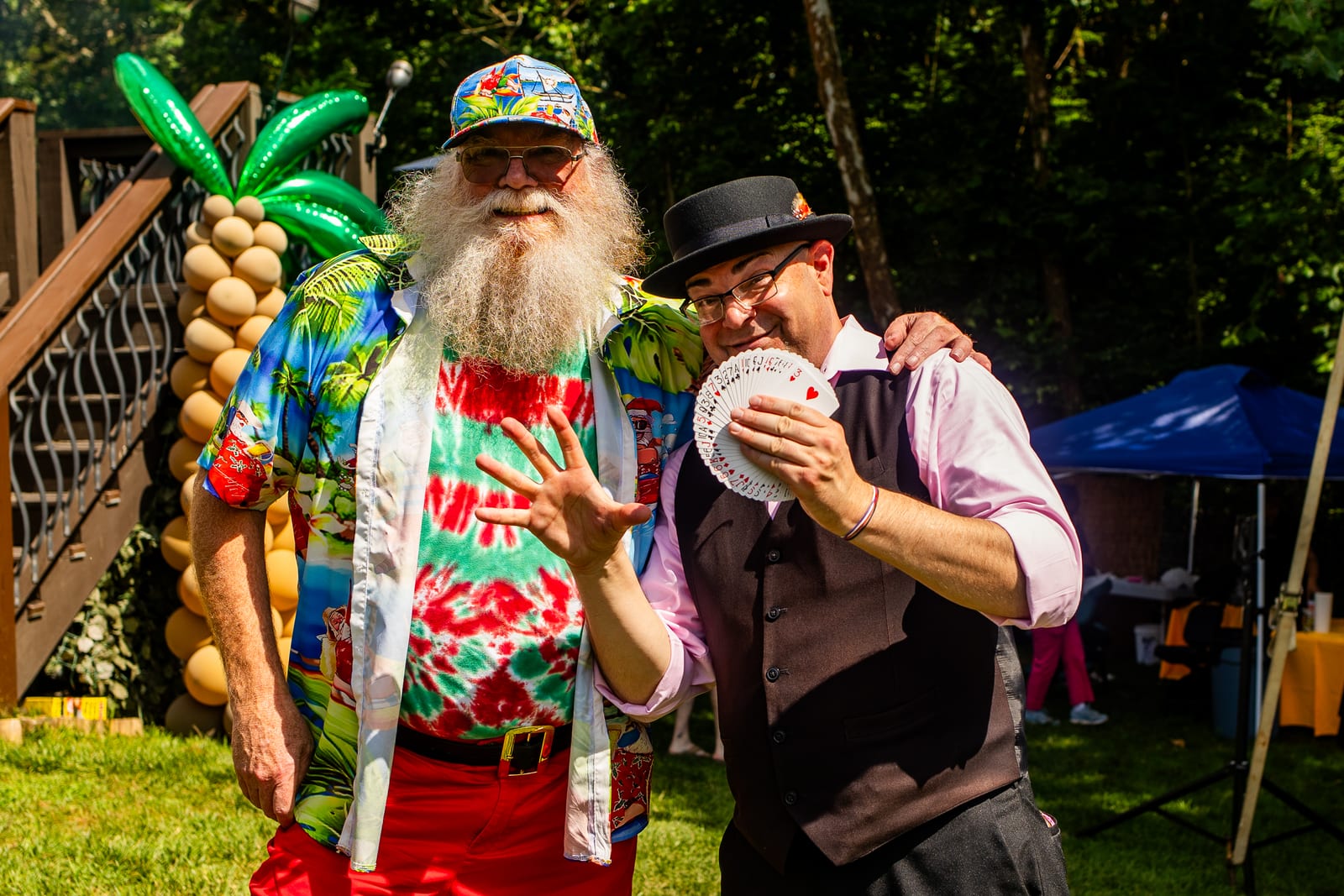 Balloon artist beside a tall balloon palm tree posing with a top-hatted magician