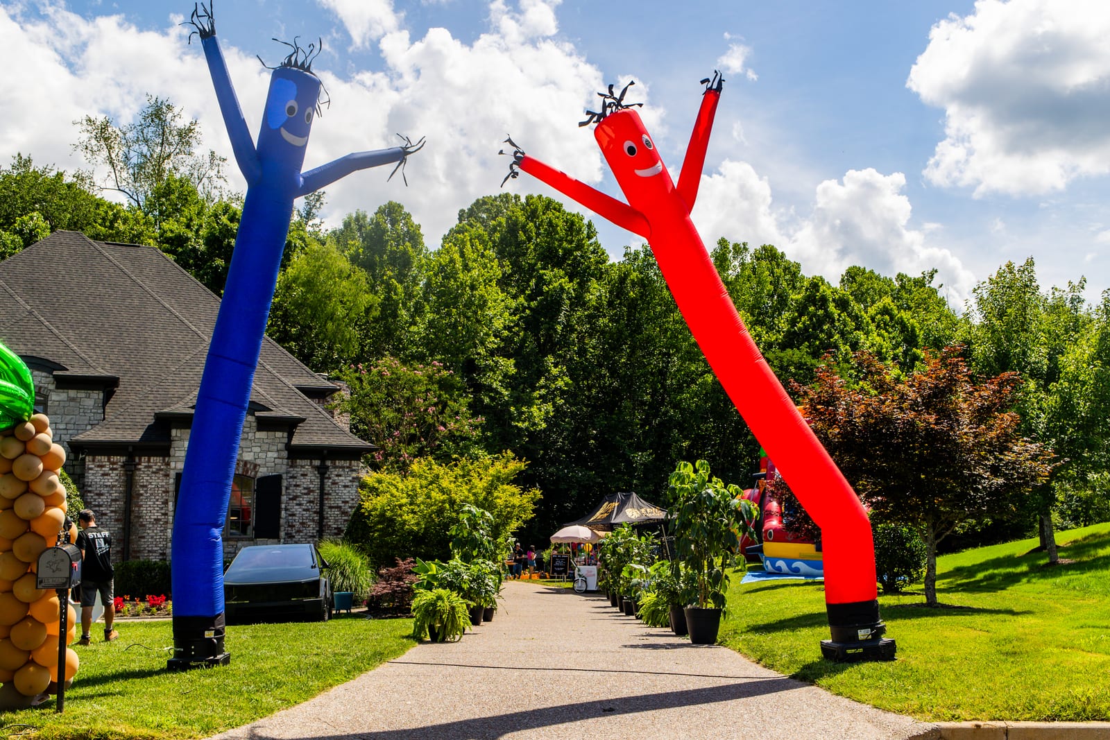 Blue and red inflatable air dancers flanking a driveway in front of a large home