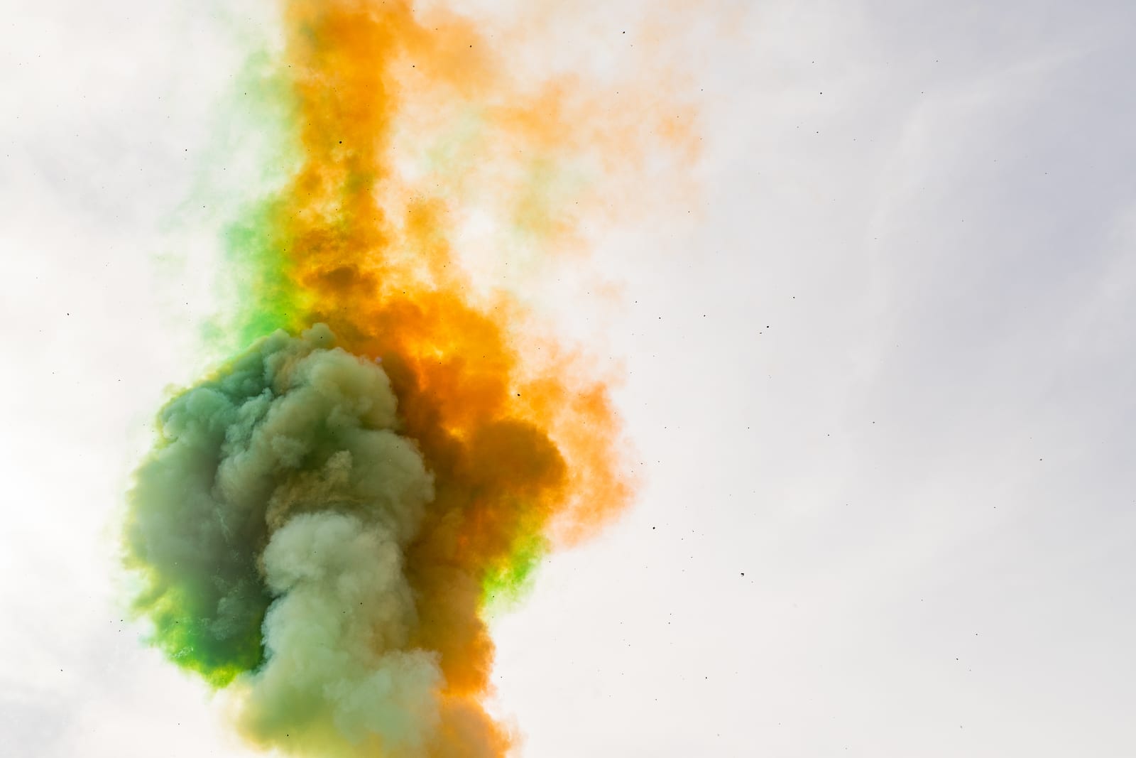 Billowing orange and green coloured smoke rising against a pale sky