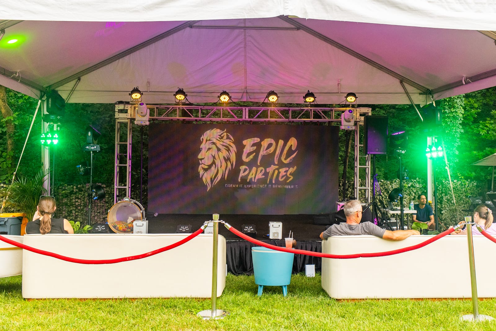 EPIC Parties branded LED stage under a marquee with green uplighting and a roped lounge