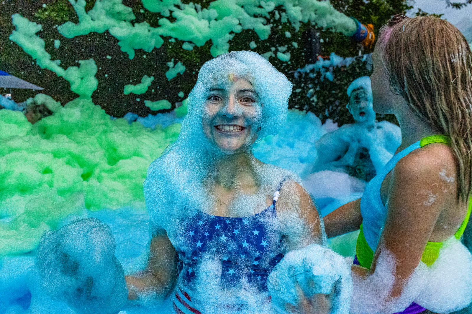 Guest grinning while covered head to toe in blue and green party foam at night