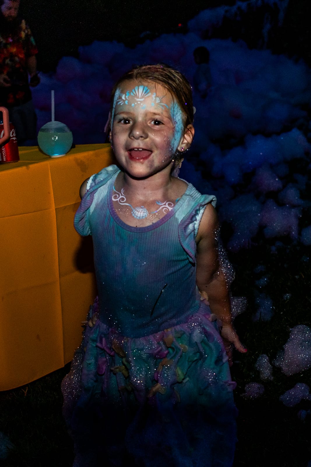 Young guest covered in glittering foam smiling in the dark