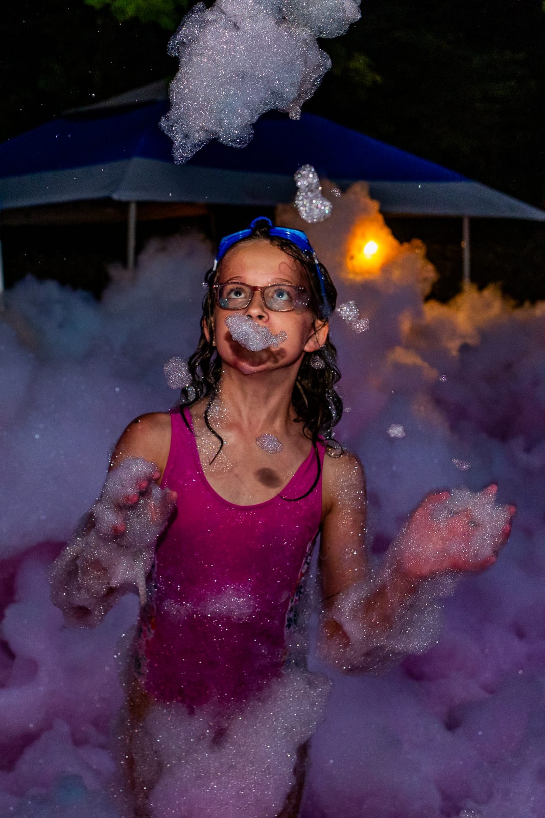 Guest wearing a tall crown of foam beneath a parasol at a night foam party
