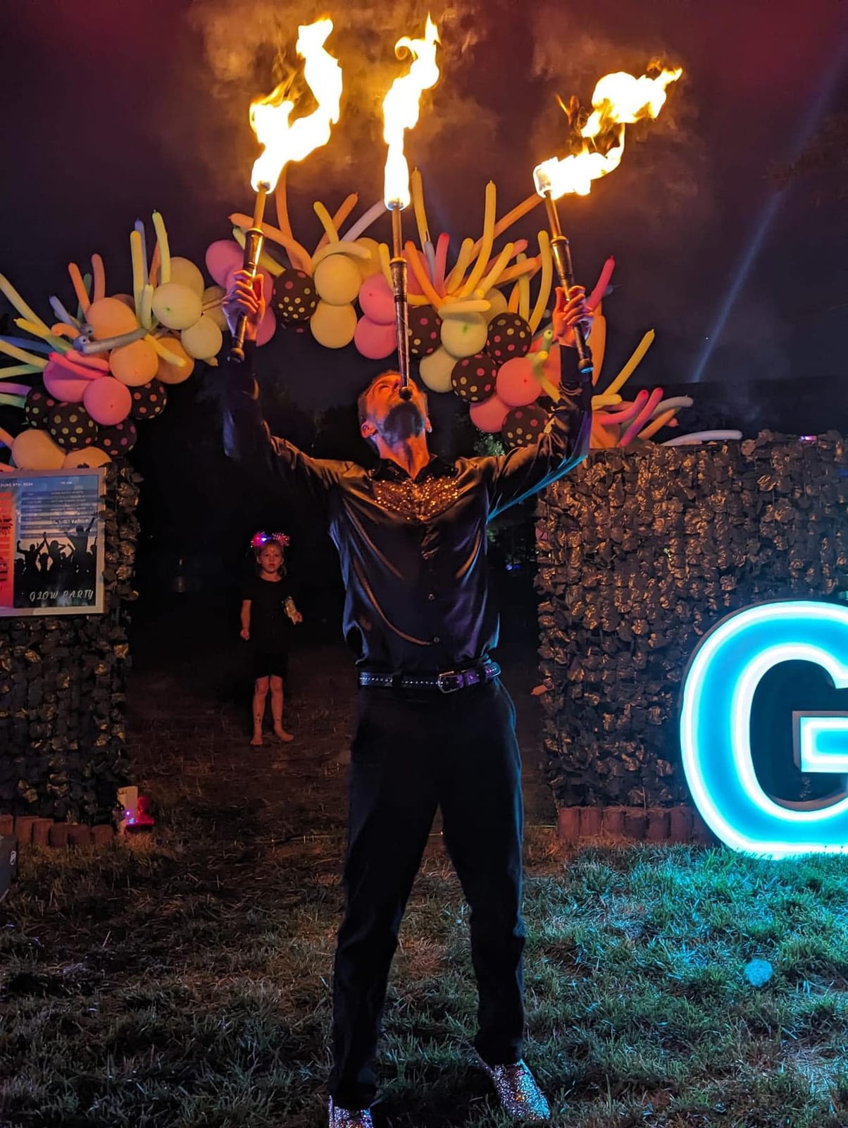 Fire performer holding a blazing multi-torch headpiece against a night sky