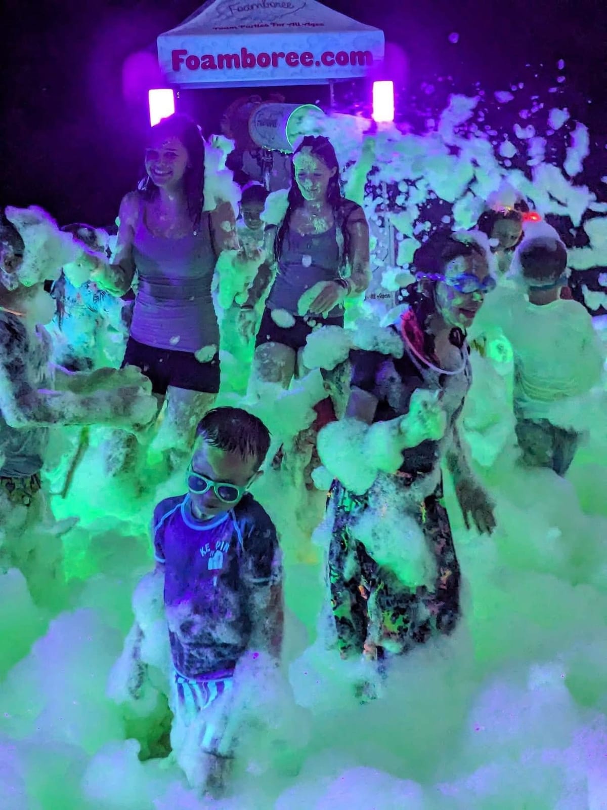Guests dancing in glowing green foam under blacklight at a night foam party