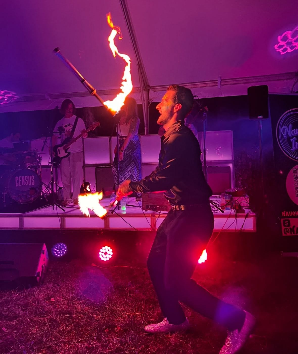 Fire performer breathing flame in front of a live band under magenta stage lighting