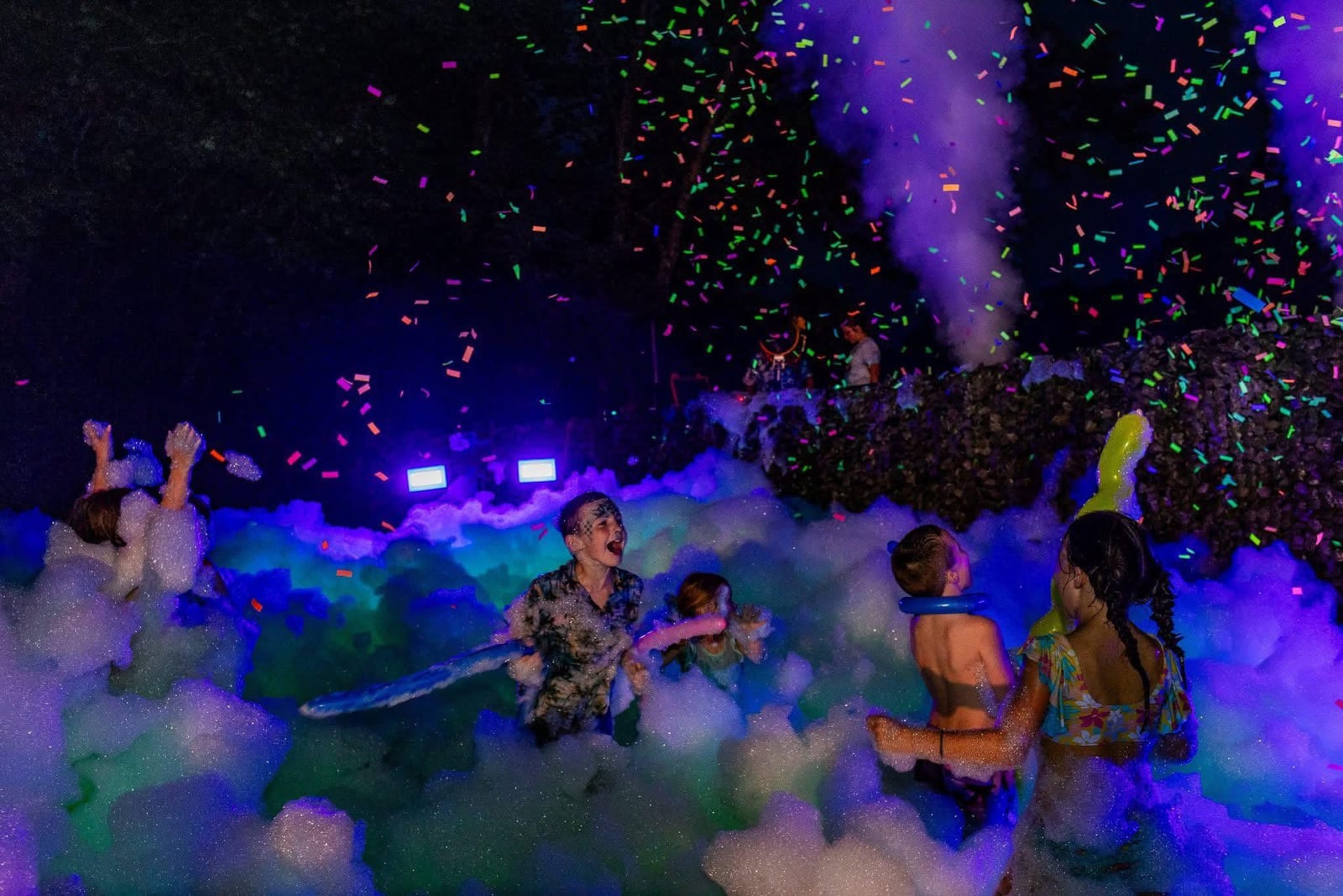 Guests in a blacklight foam pit at night with confetti falling under purple light