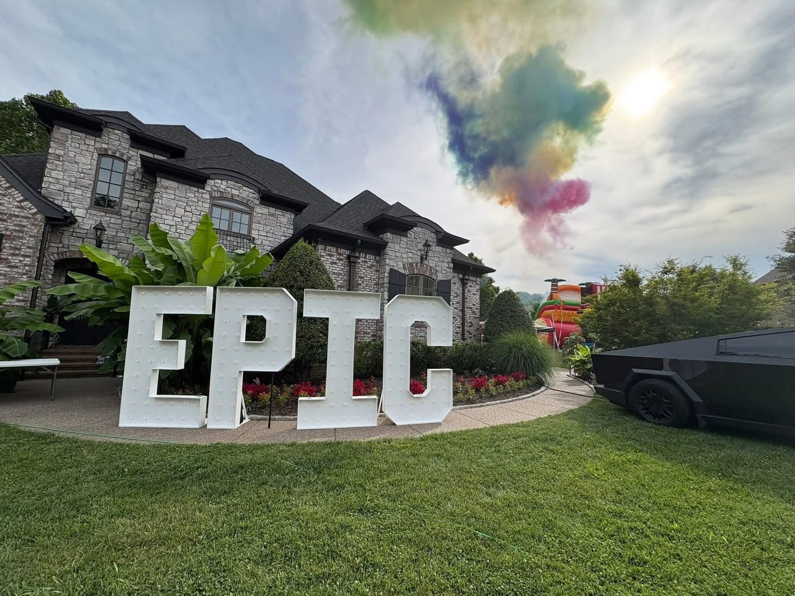 Giant white EPIC marquee letters on a lawn with colored smoke rising behind a stone house