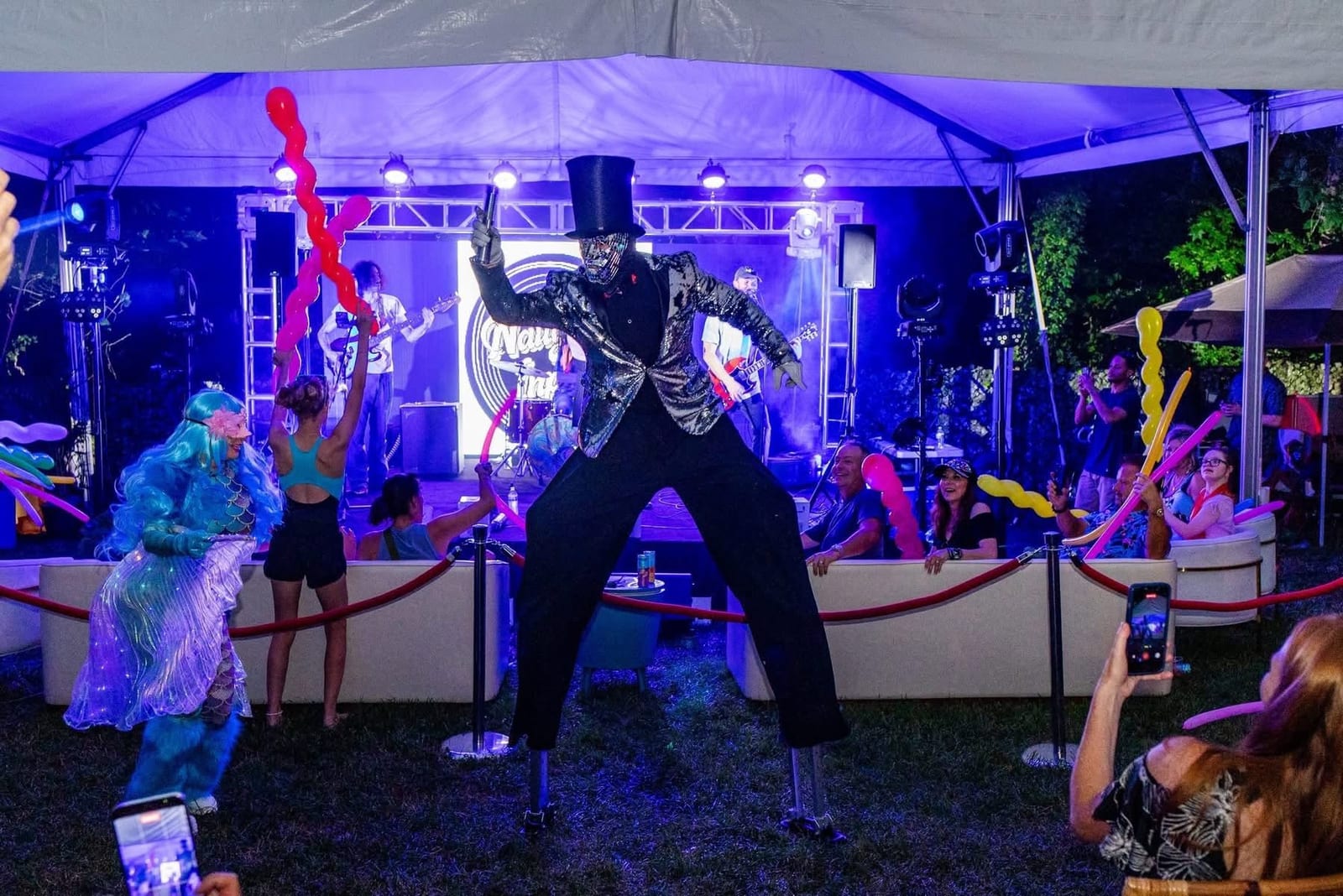 Performer in a mirrored costume on a purple-lit stage in front of seated guests