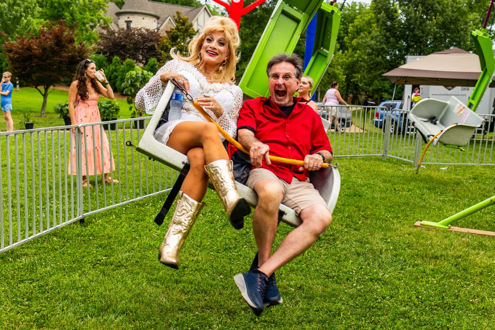 Costumed performer in a blonde wig riding a fairground swing with a guest