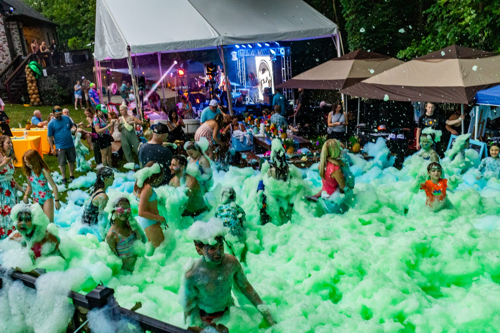 Wide view of a green foam party filling a lawn in front of a marquee stage