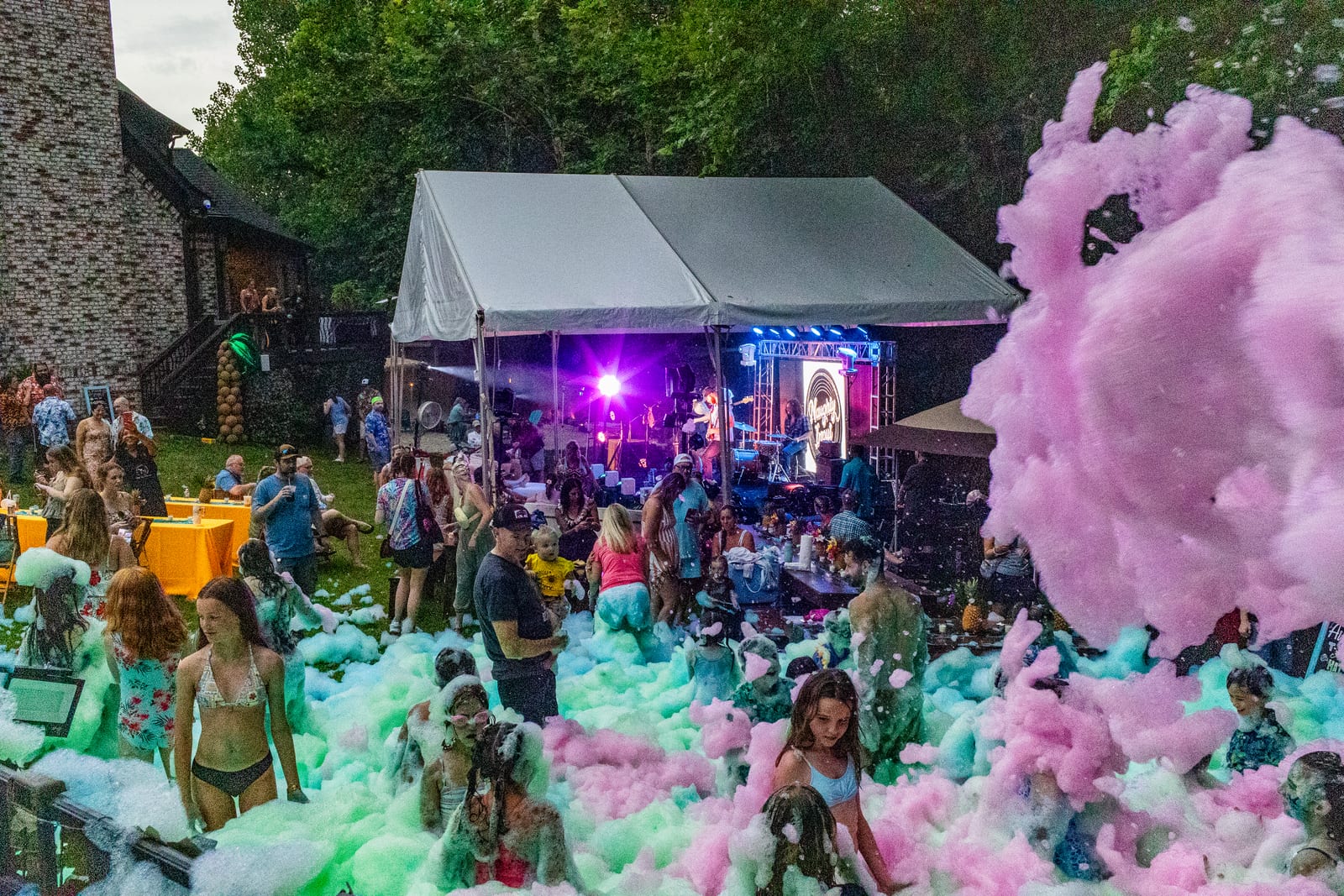 Wide view of a pink foam party on a lawn with a marquee stage and guests