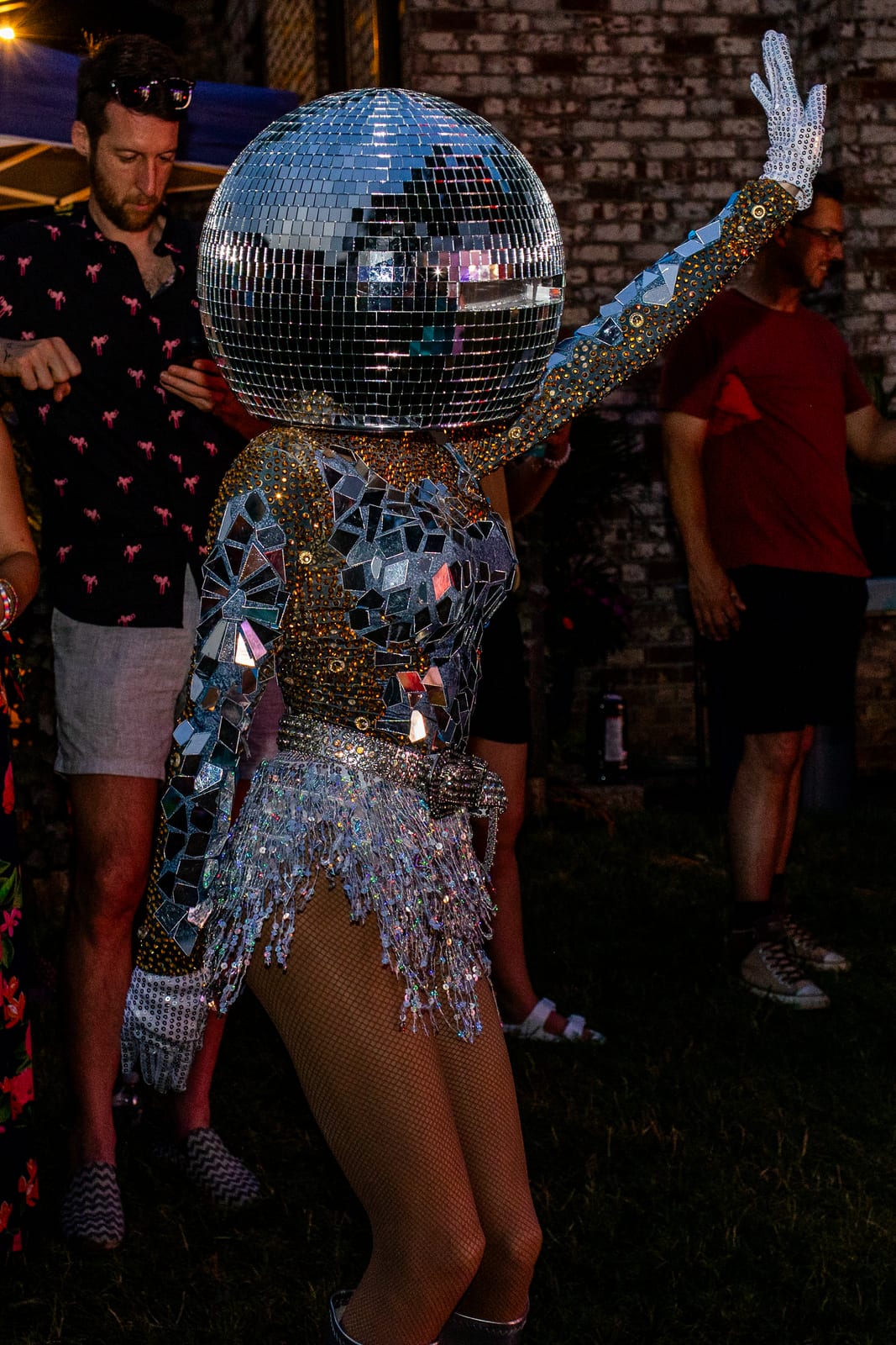 Performer in a mirrored costume with a mirror-ball head greeting guests at dusk