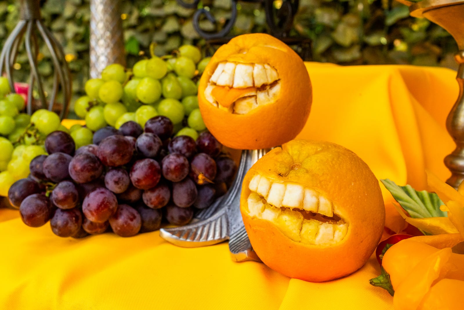 Carved oranges shaped into faces beside grapes on a yellow cloth
